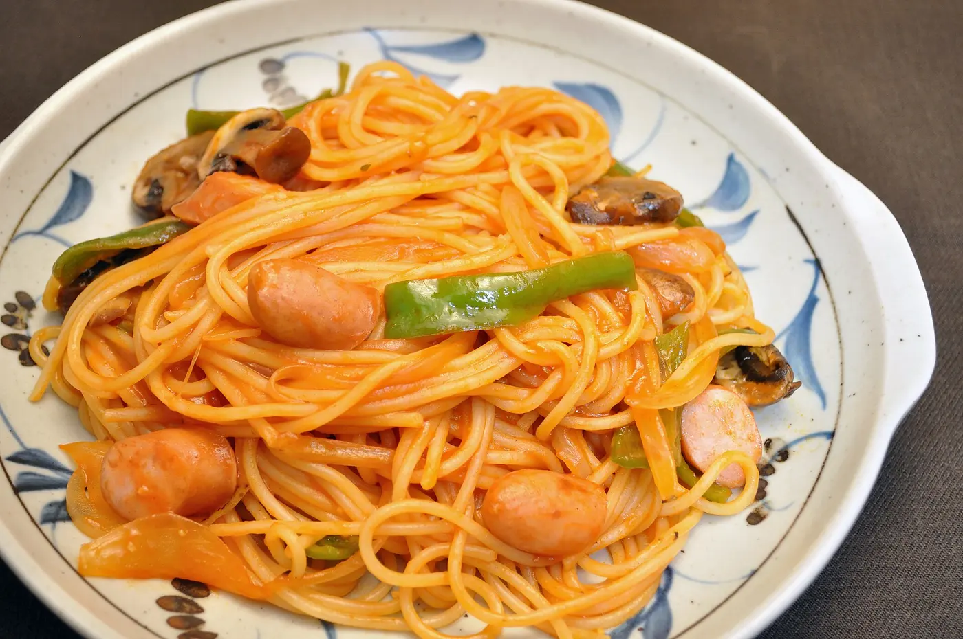 Orange spaghetti on a blue-and-white patterned plate, mixed with sausage, green pepper, mushrooms and onion