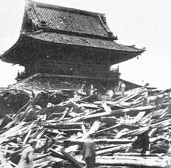 An old black-and-white photo of the timbers of a collapsed building piled up in front of a large temple hall with a tiled roof