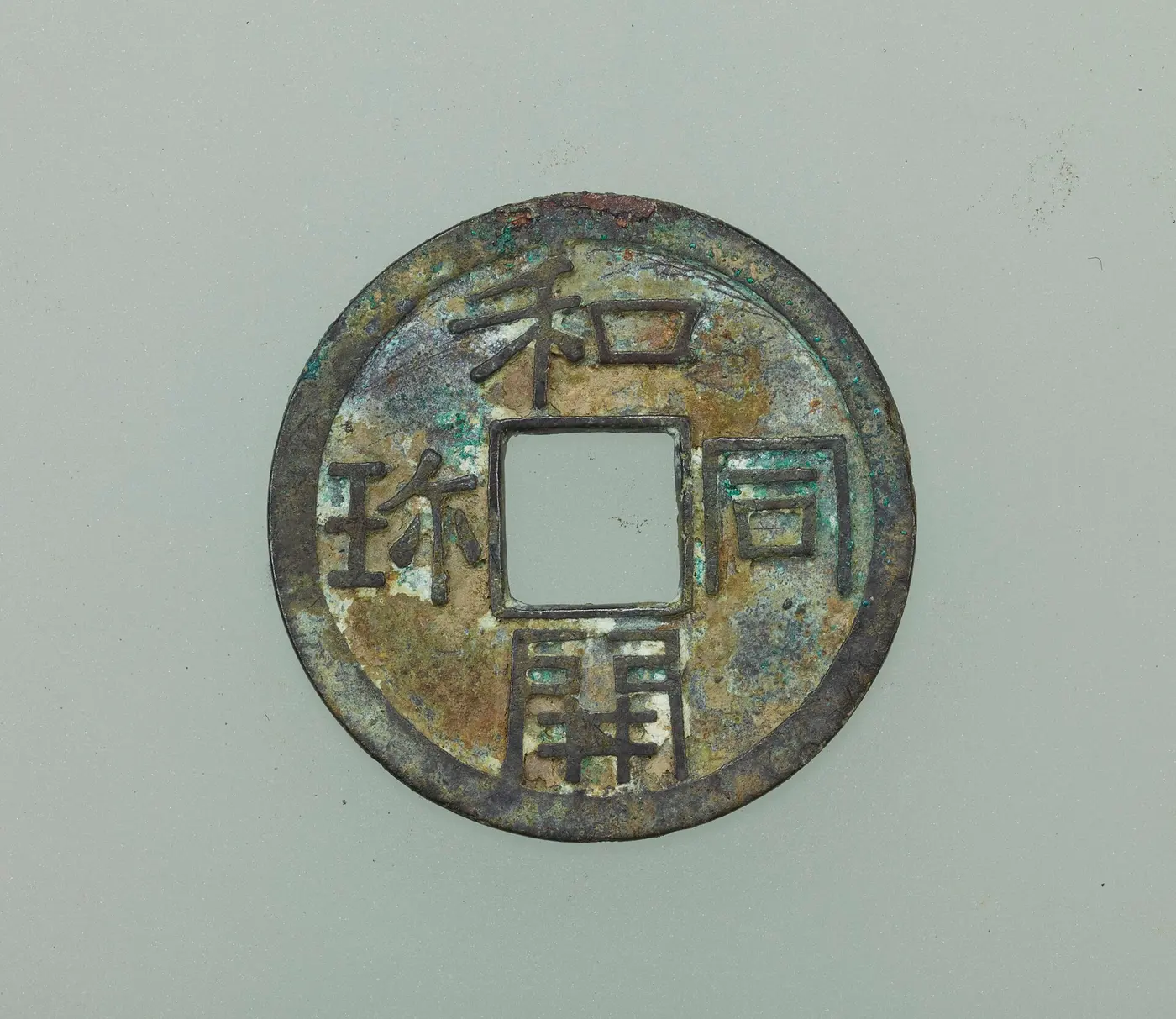 A copper coin with the four characters of “Wadō kaichin” arranged around a square hole