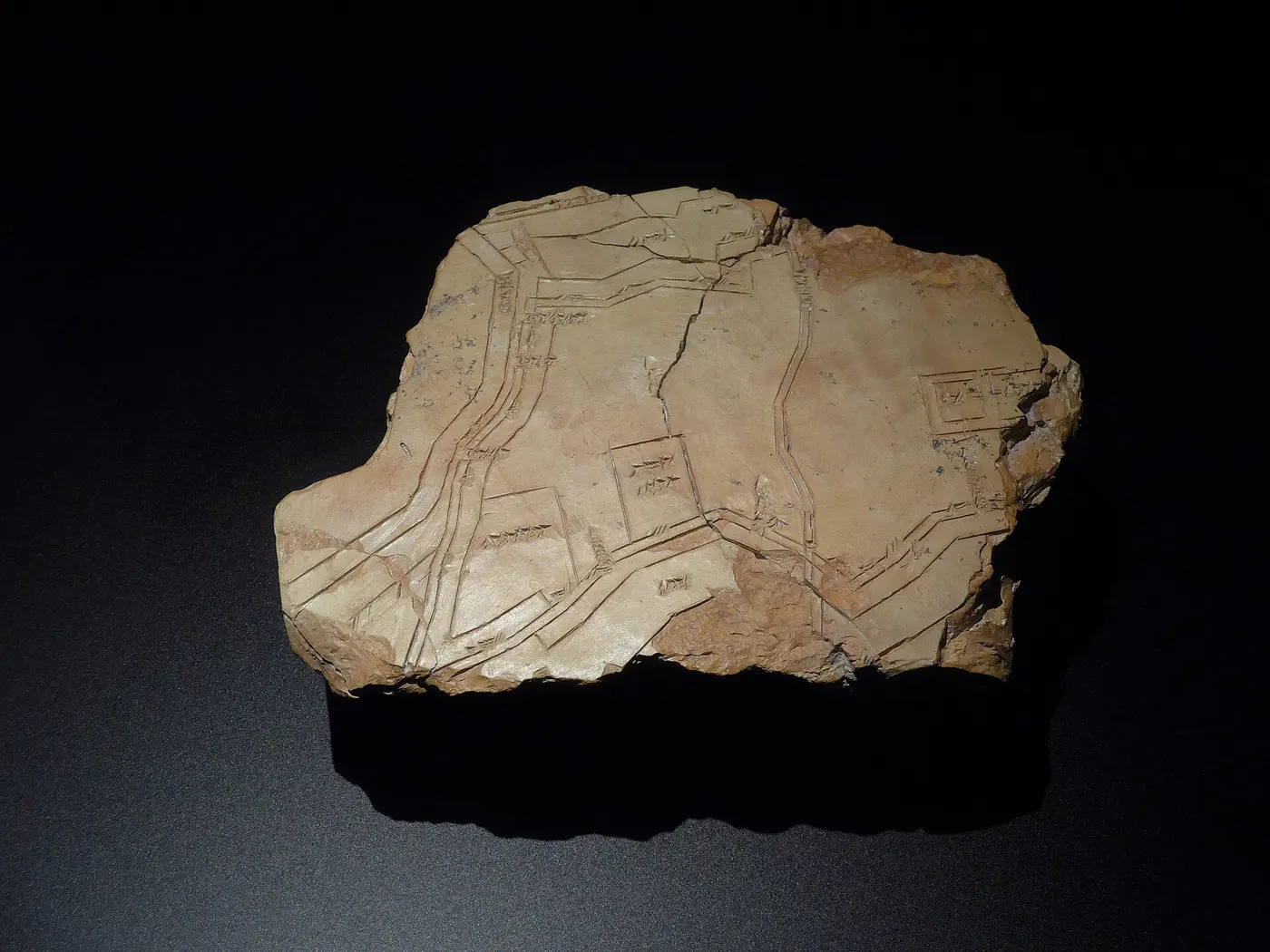 A fragment of a clay tablet carved with lines representing walls, canals and buildings, along with cuneiform writing