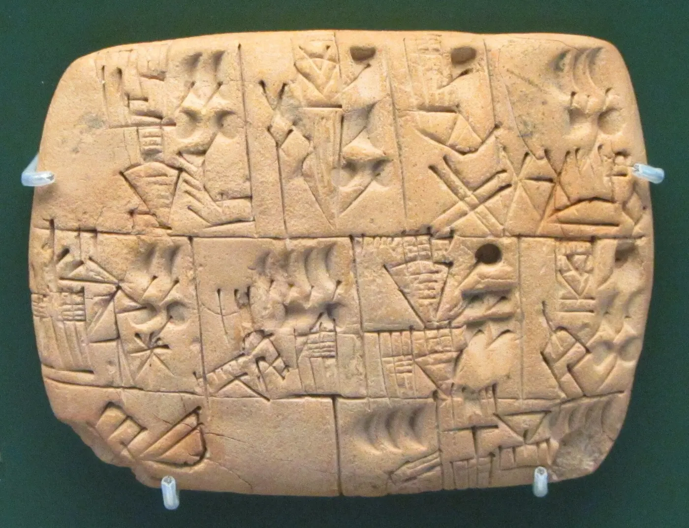 A clay tablet divided into boxes, inscribed with picture-like signs and round impressions representing numbers