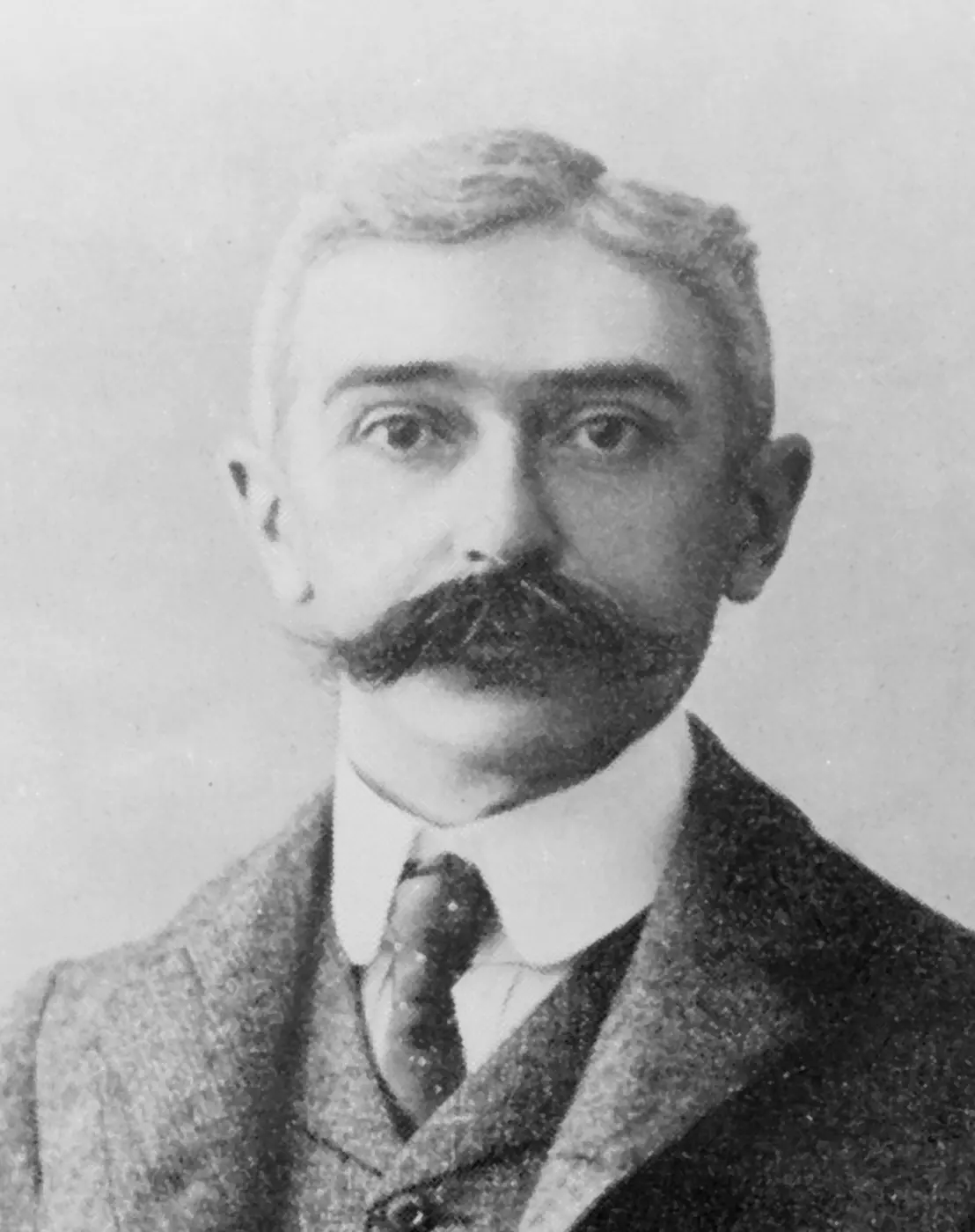 Portrait photograph of Pierre de Coubertin in a suit, with a large mustache