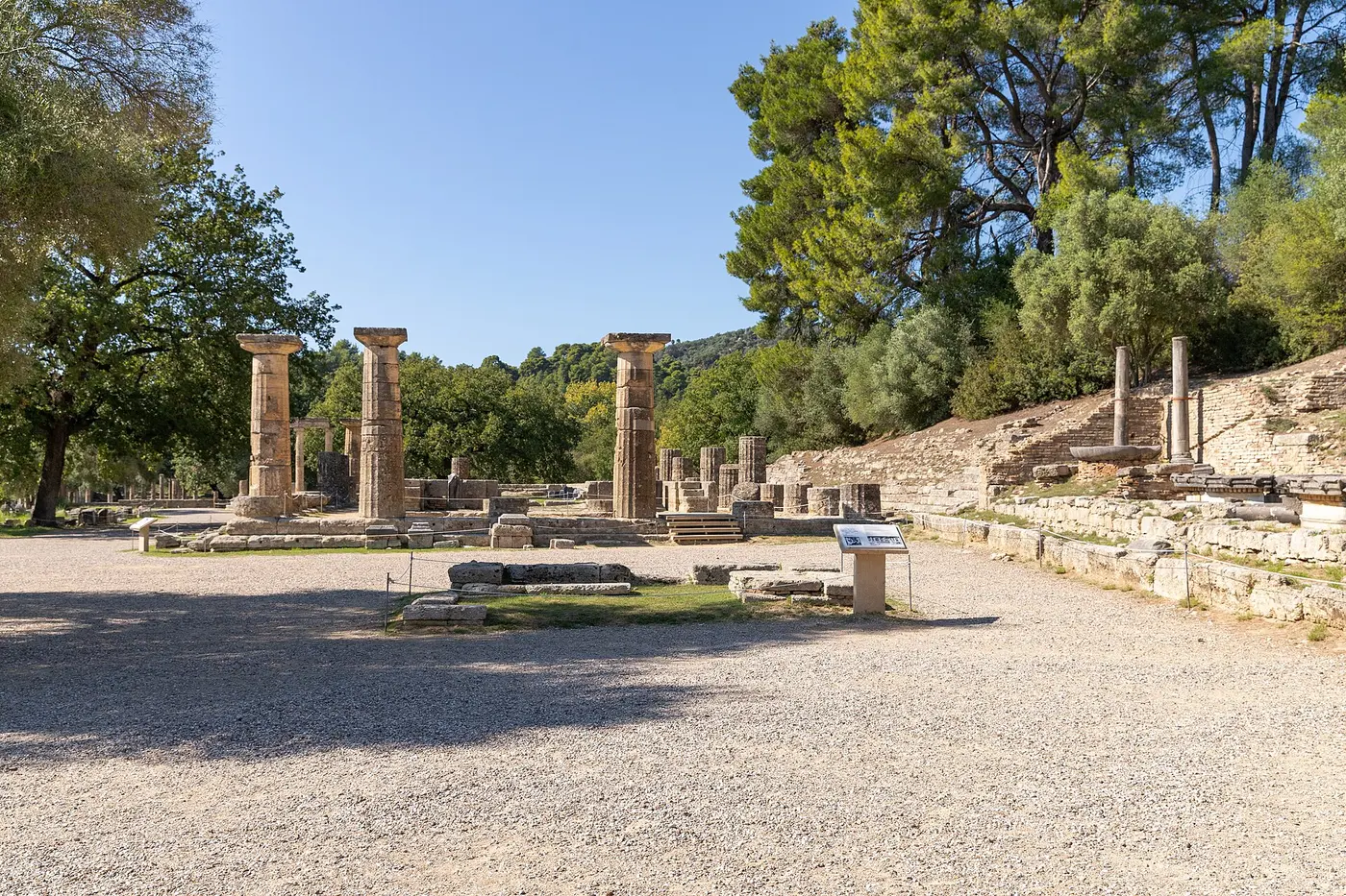 Ancient ruins with several stone columns standing among trees under a blue sky