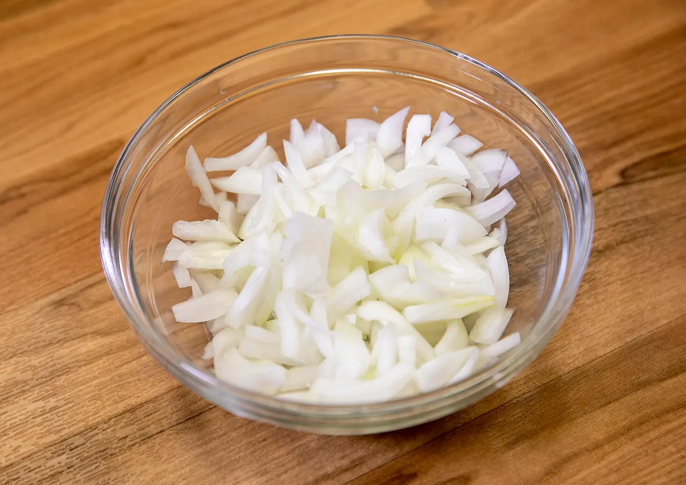 Sliced white onions in a glass bowl on a wooden table