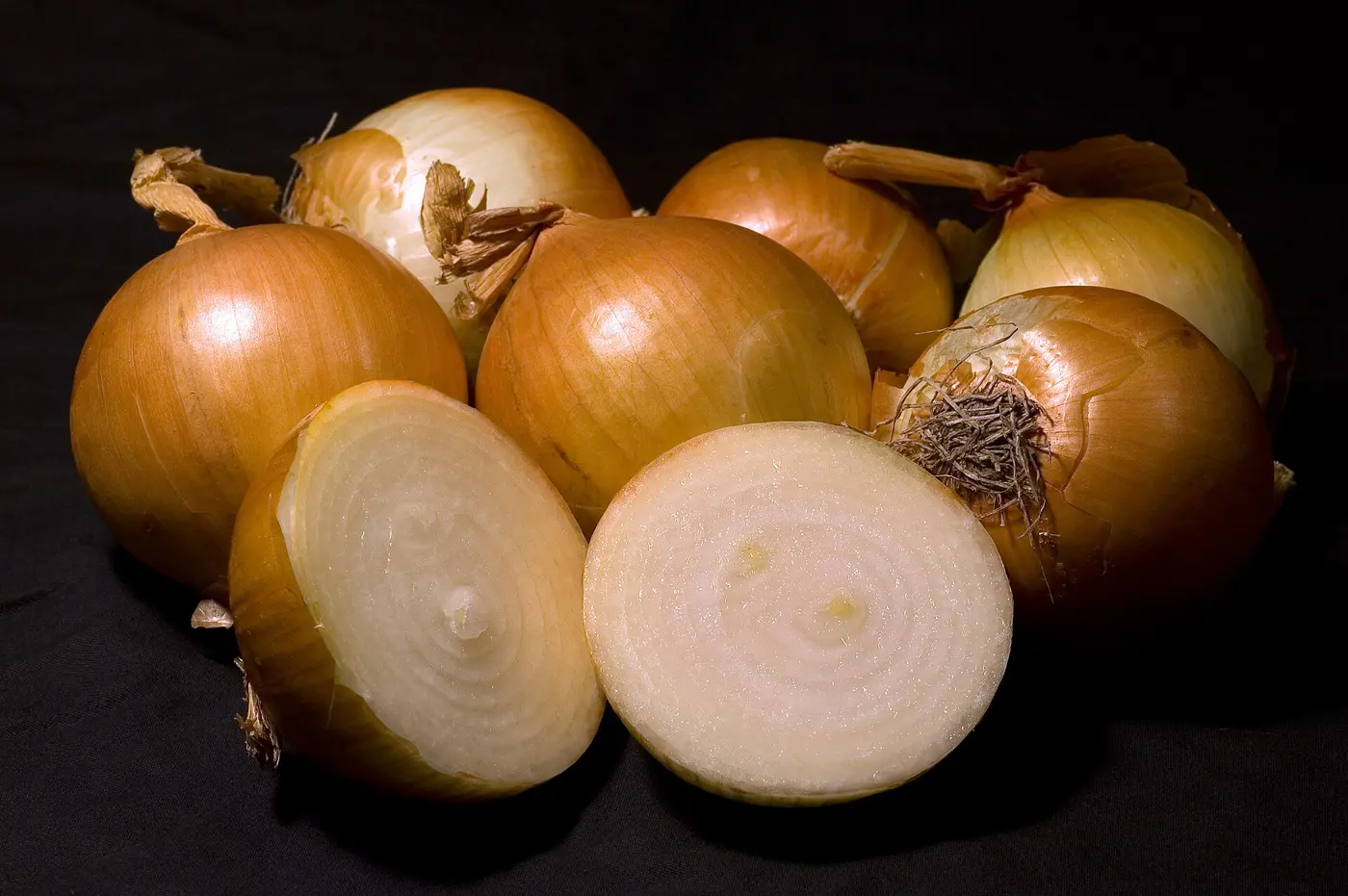 A whole onion and an onion cut in half to show its cross-section, against a black background