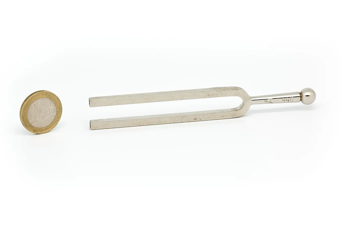 A metal tuning fork stamped with 440, lying next to a one-euro coin