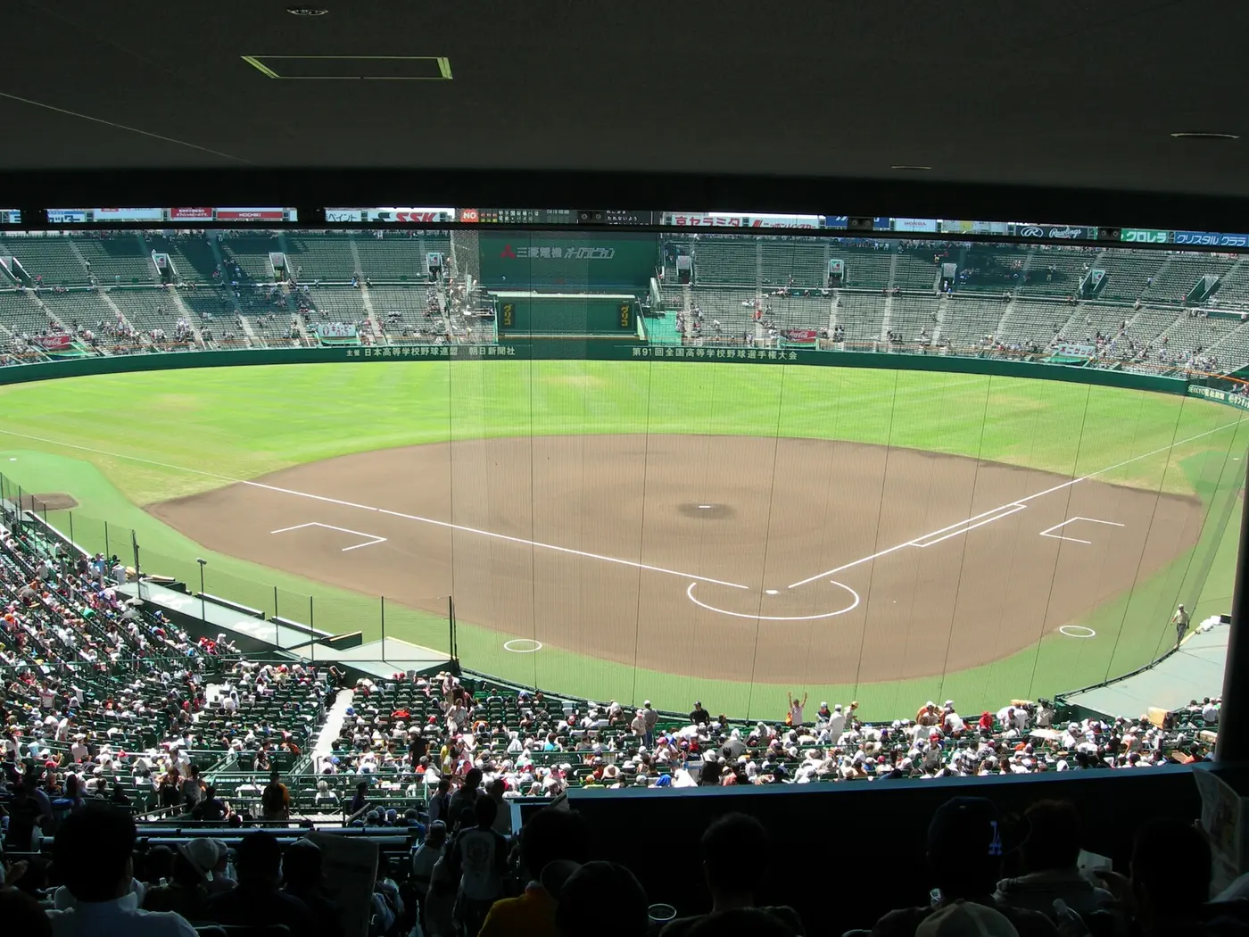 A view from high in the stands of a baseball field with a dirt infield and green grass at Koshien Stadium