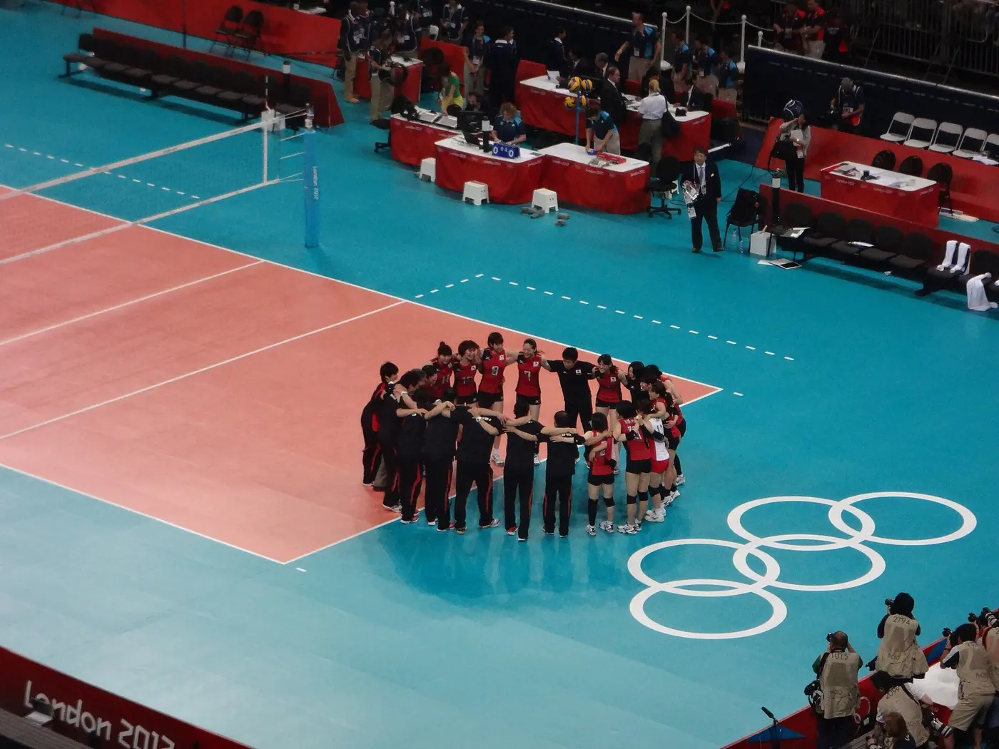 Players standing in a tight circle with their arms around each other on a volleyball court