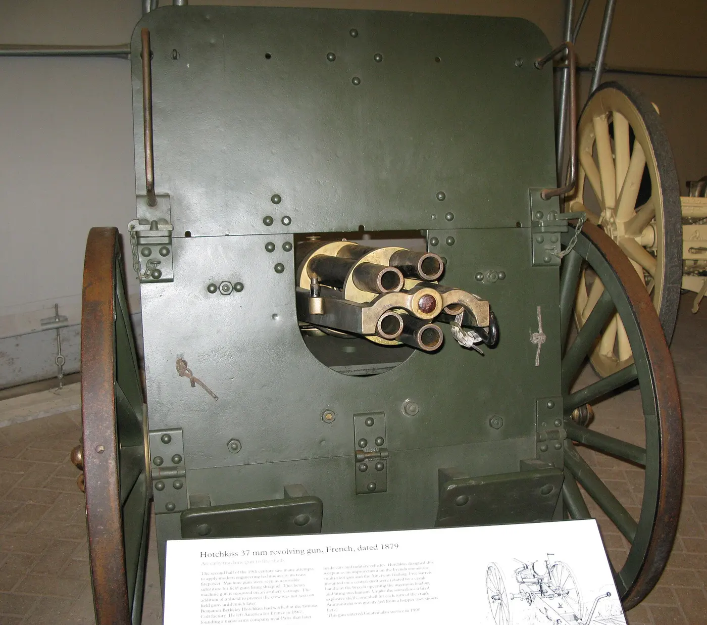 An old cannon with five bundled barrels poking out from the center of a green, wheeled gun shield
