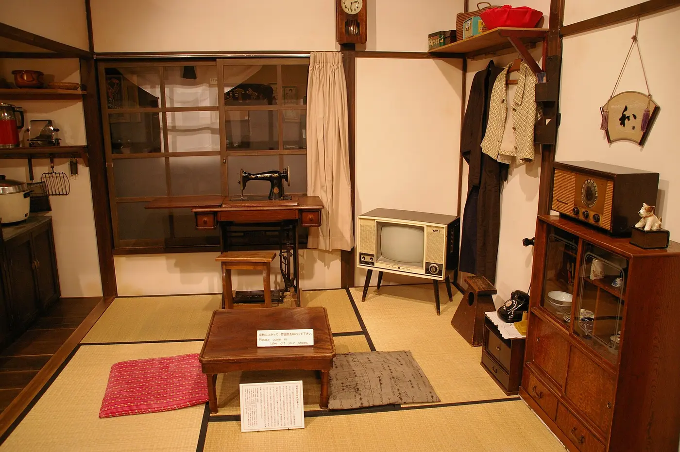 A re-created room with tatami mats, a wooden low table and floor cushions in the center, and a sewing machine and television along the back