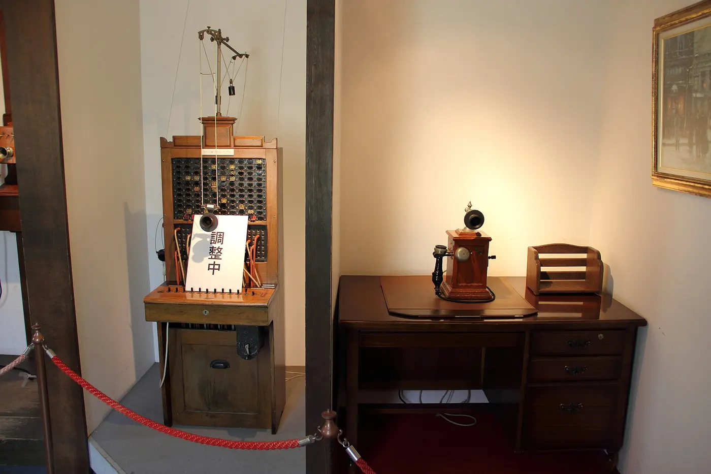An old wooden telephone switchboard and a telephone on a desk, displayed in a museum room