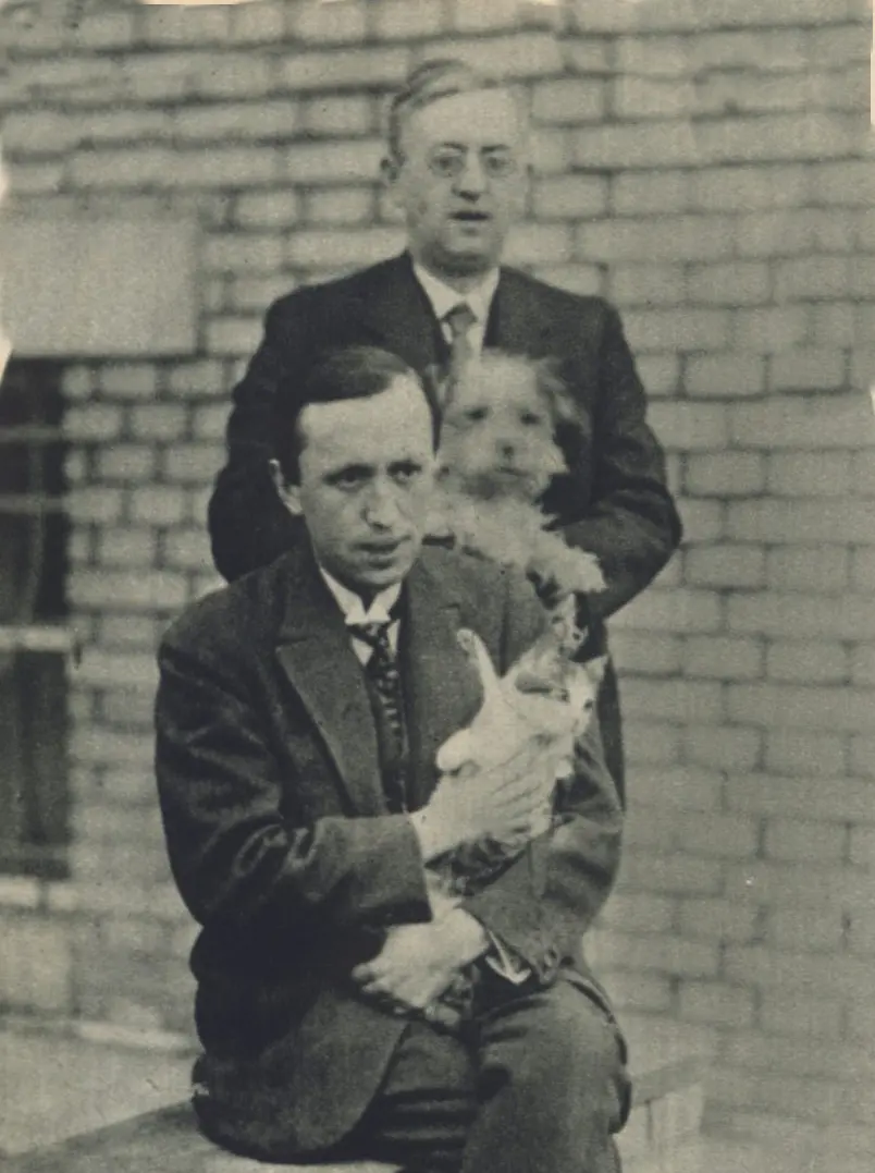 The brothers Karel and Josef Čapek posing in front of a brick wall, holding a dog and a cat