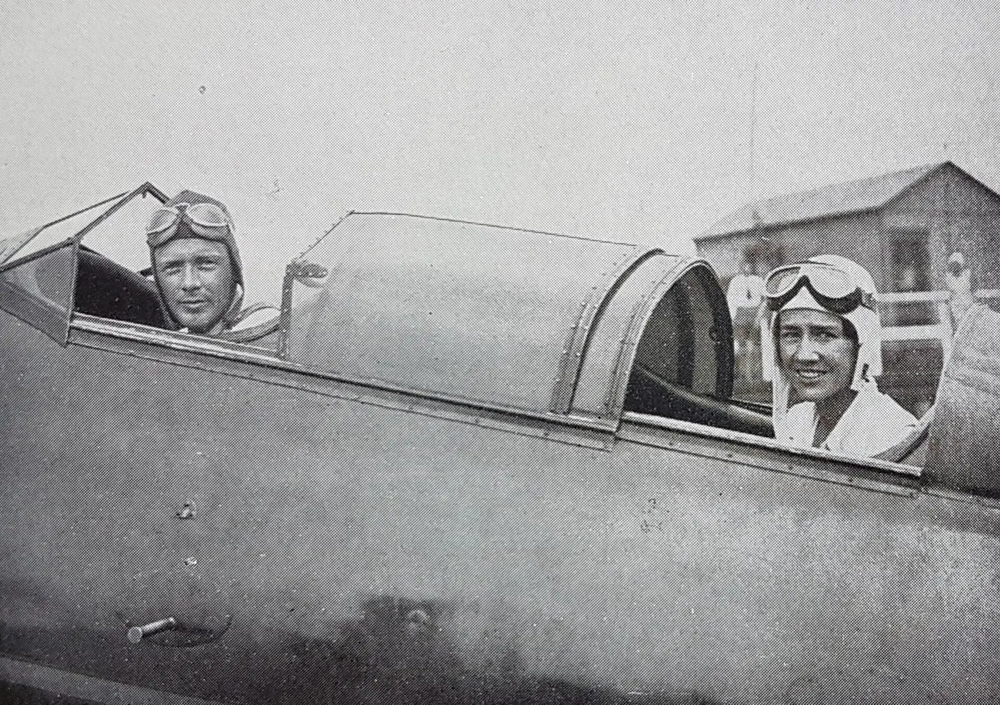 Black-and-white photo of Charles and Anne Lindbergh in flight helmets and goggles, looking out from an airplane cockpit