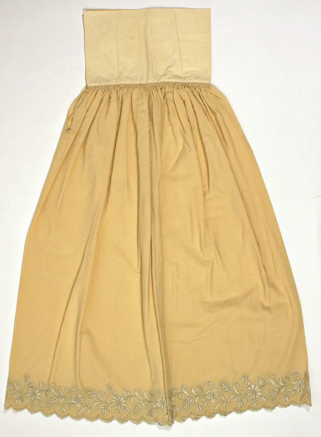 A long pale-yellow petticoat with a waistband at the top and floral embroidery along the hem