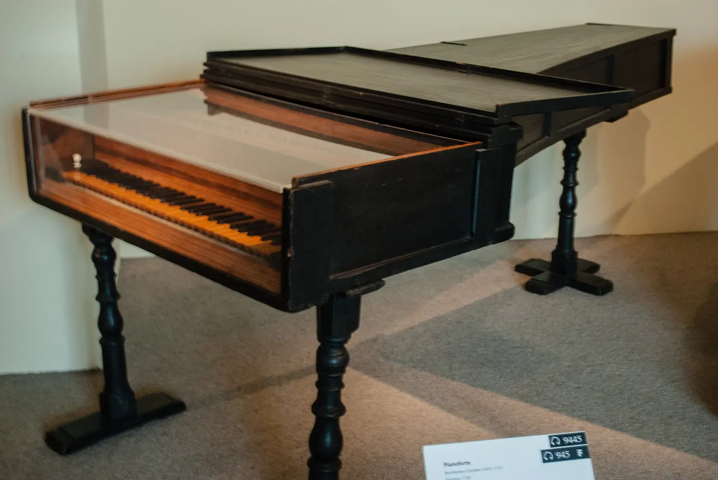 An early piano with a long, narrow wooden case on display in a gallery