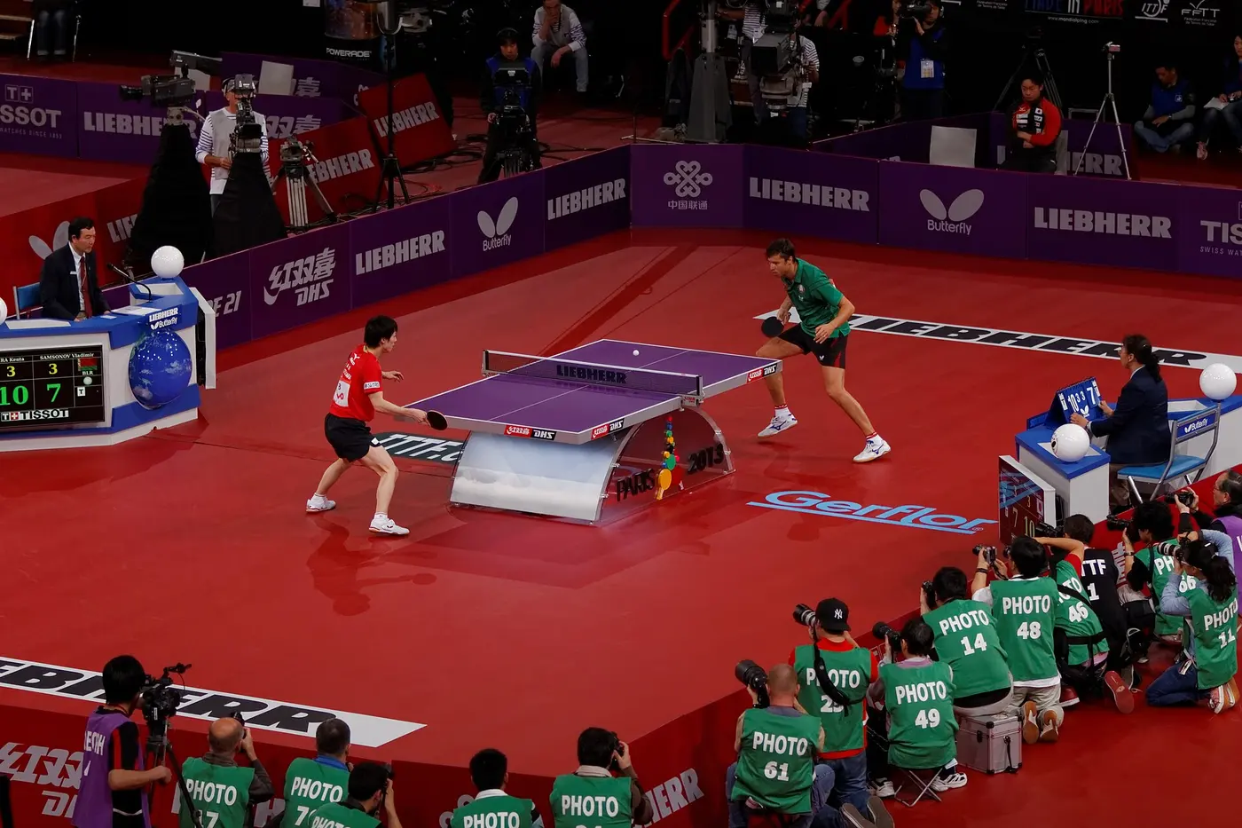 Two players rallying across a table tennis table in a large arena