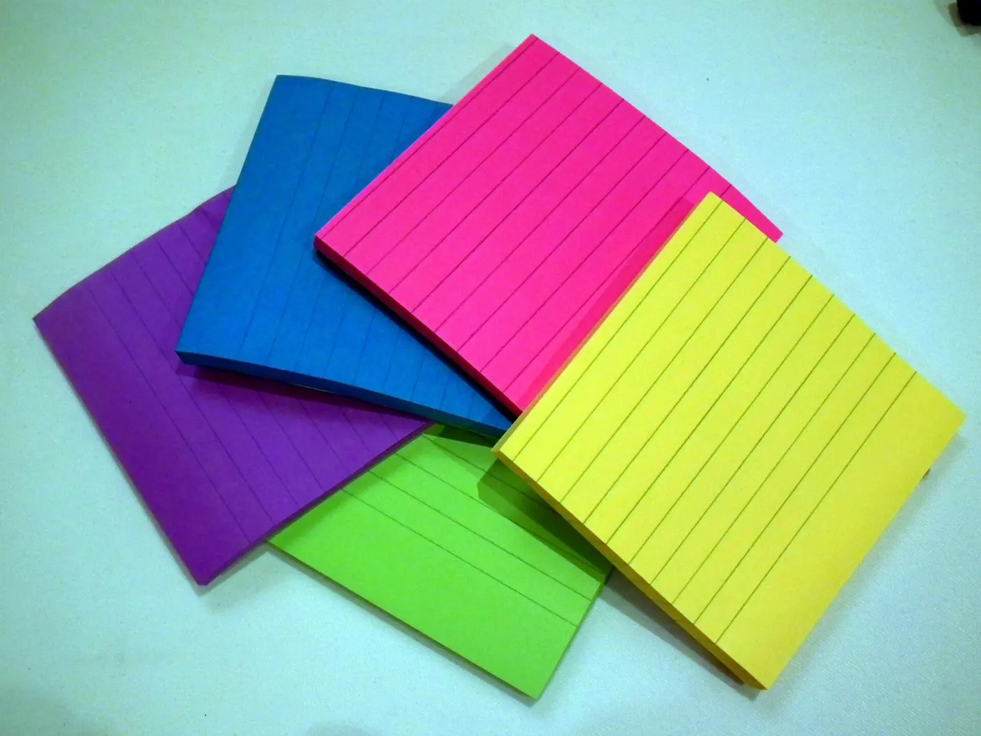 Stacks of lined sticky notes in purple, blue, pink, green and yellow, piled on top of each other