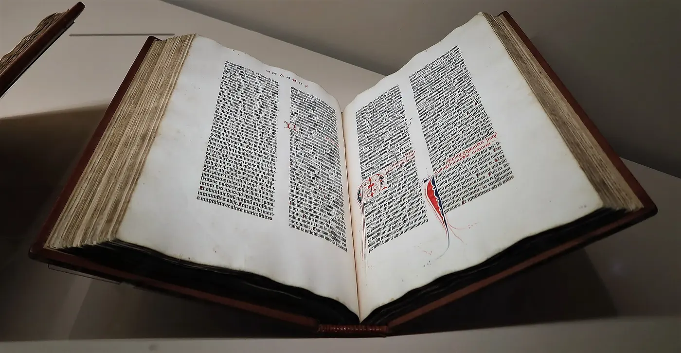 A large old book lying open, both pages densely printed with Latin text in two columns and decorated with red initials