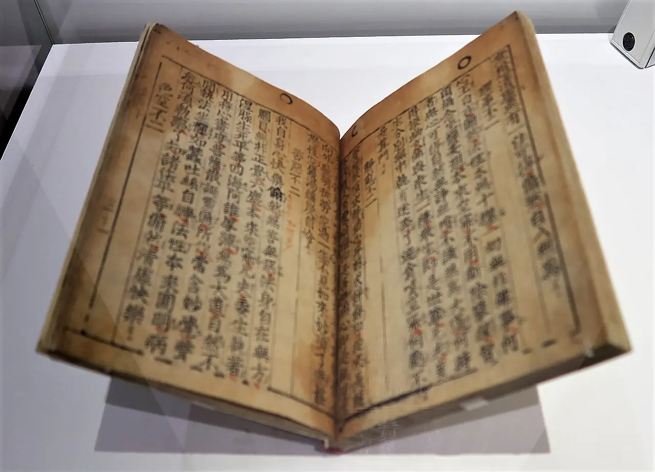 An old book lying open in a display case, its browned pages densely filled with vertical columns of Chinese characters