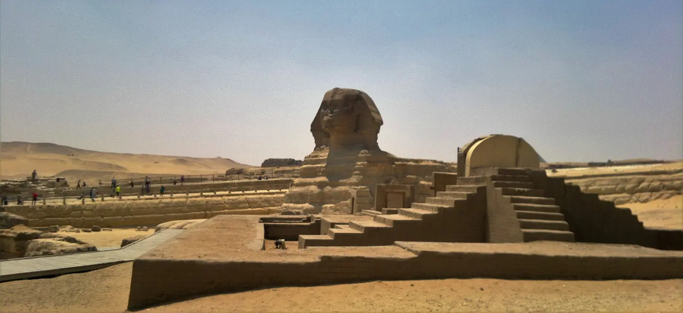 The Great Sphinx crouching on a desert plateau, with stone ruins spread out in the foreground