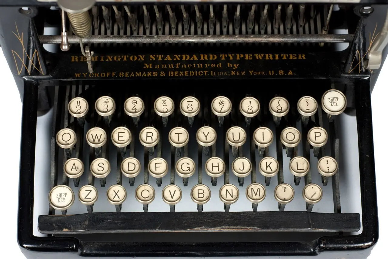A black typewriter with four rows of round white keys, the second row showing the letters Q, W, E, R, T, Y