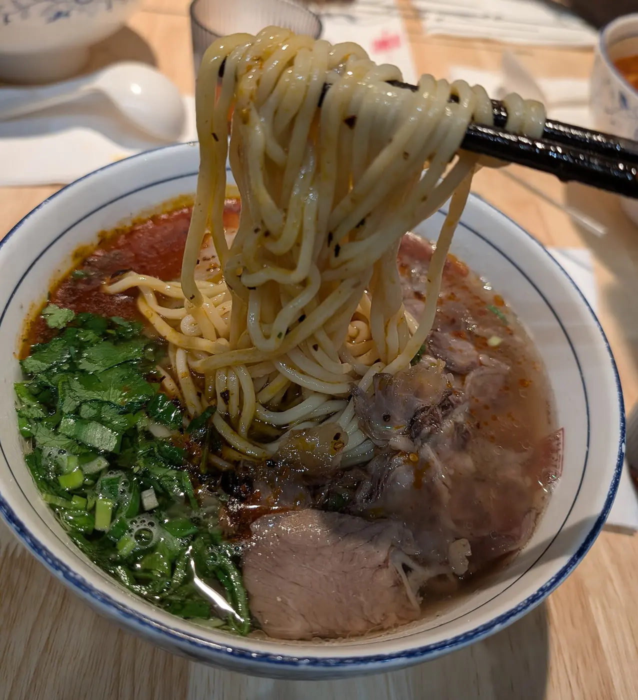 Chopsticks lifting white noodles from a bowl of soup topped with beef and cilantro
