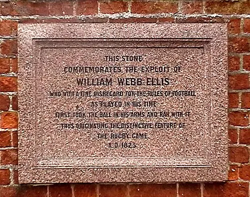 A stone tablet set into a brick wall, engraved in English with the name William Webb Ellis and the date A.D. 1823