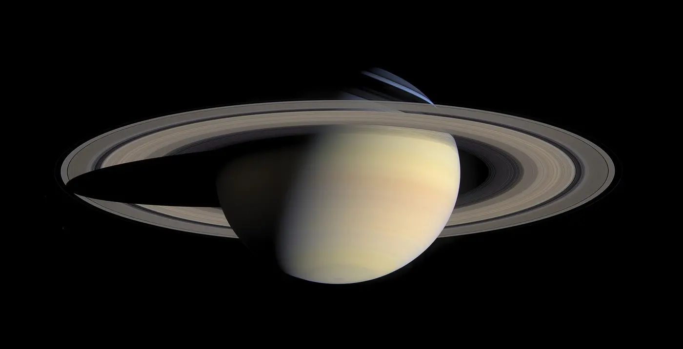 Saturn with pale yellow bands and its broad rings sweeping diagonally, the planet’s shadow falling across the rings