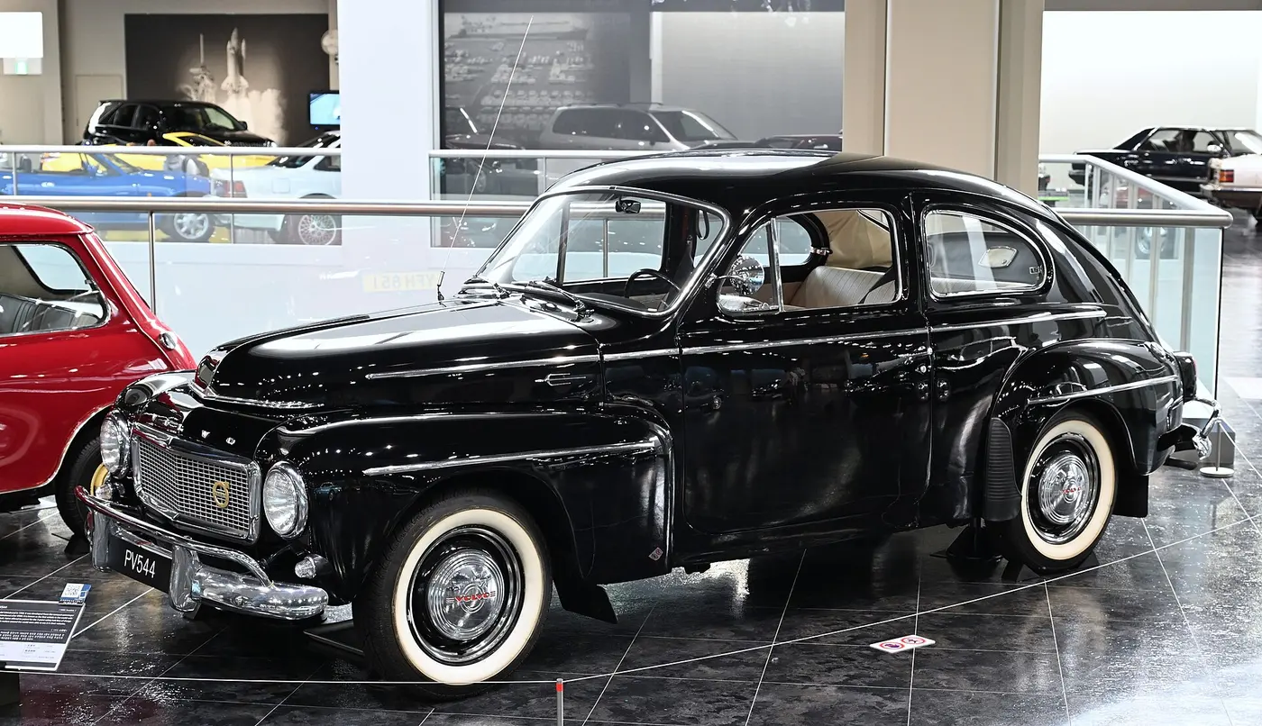 A rounded black classic car on display on a museum floor