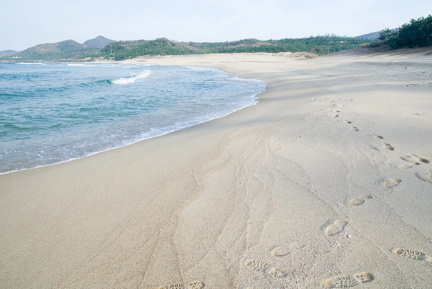 Blue waves washing up on a pale sandy beach marked with footprints