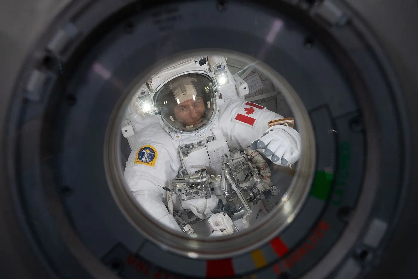 An astronaut in a white spacesuit looking out through a round window