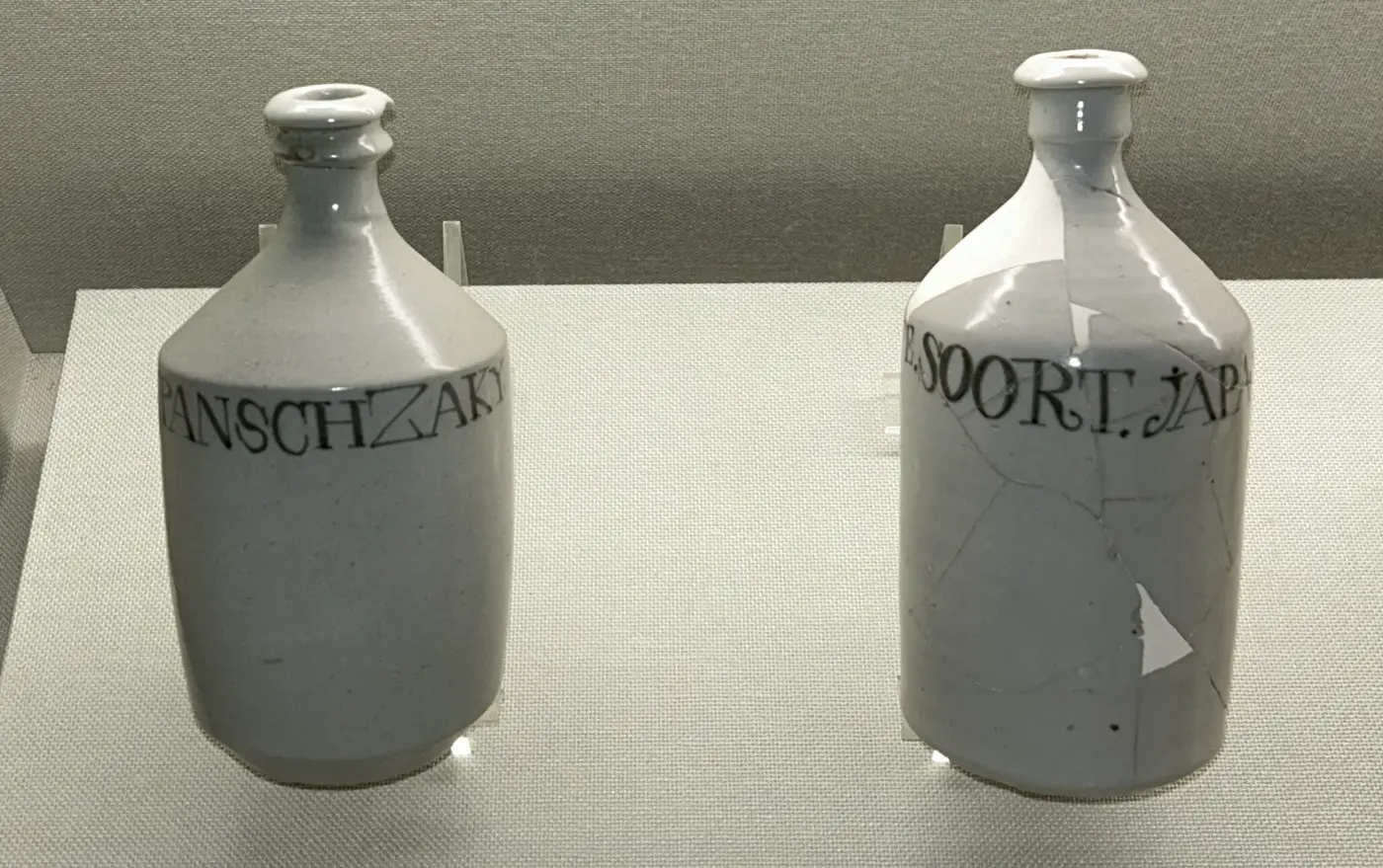 Two white porcelain bottles in a display case, each with lettering in the Latin alphabet around the body