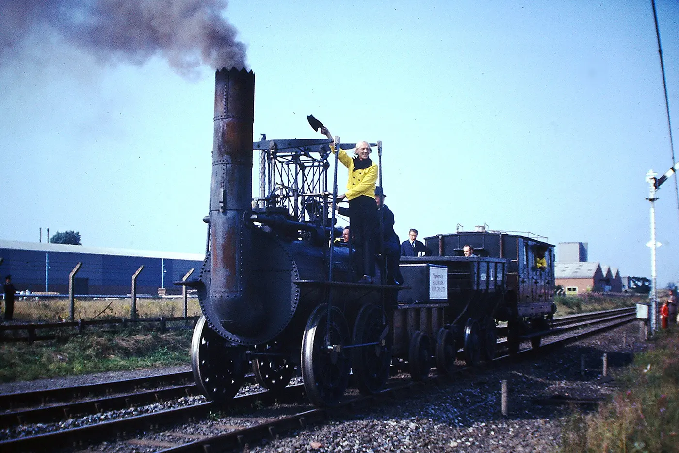 An old steam locomotive with a tall chimney running along a track with people aboard