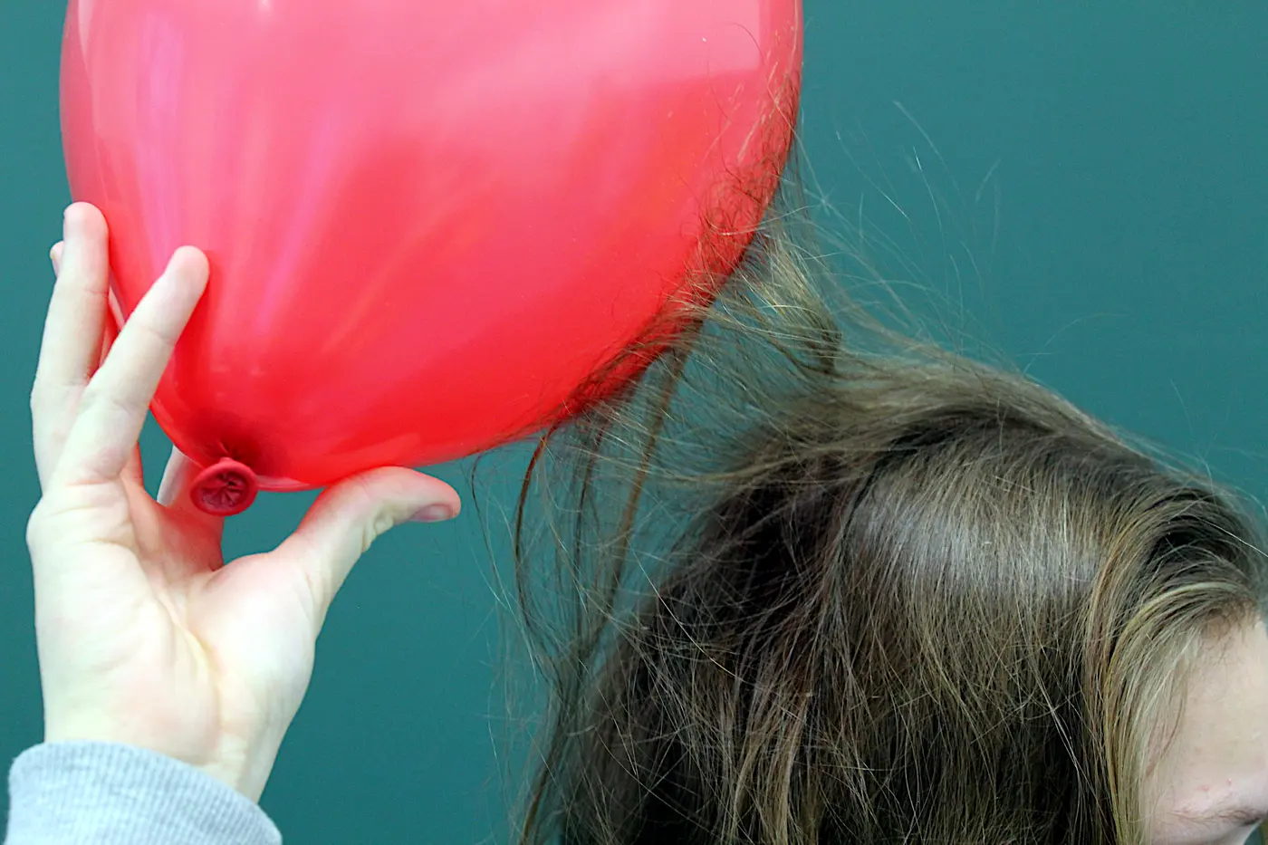 A red balloon held in a hand, with strands of hair lifting up toward it