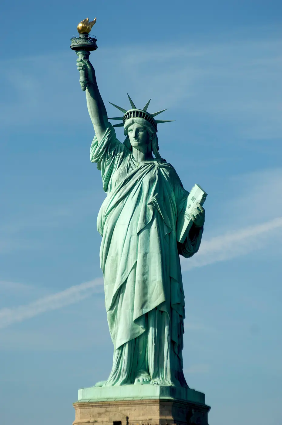 The blue-green Statue of Liberty holding up a golden torch against a blue sky