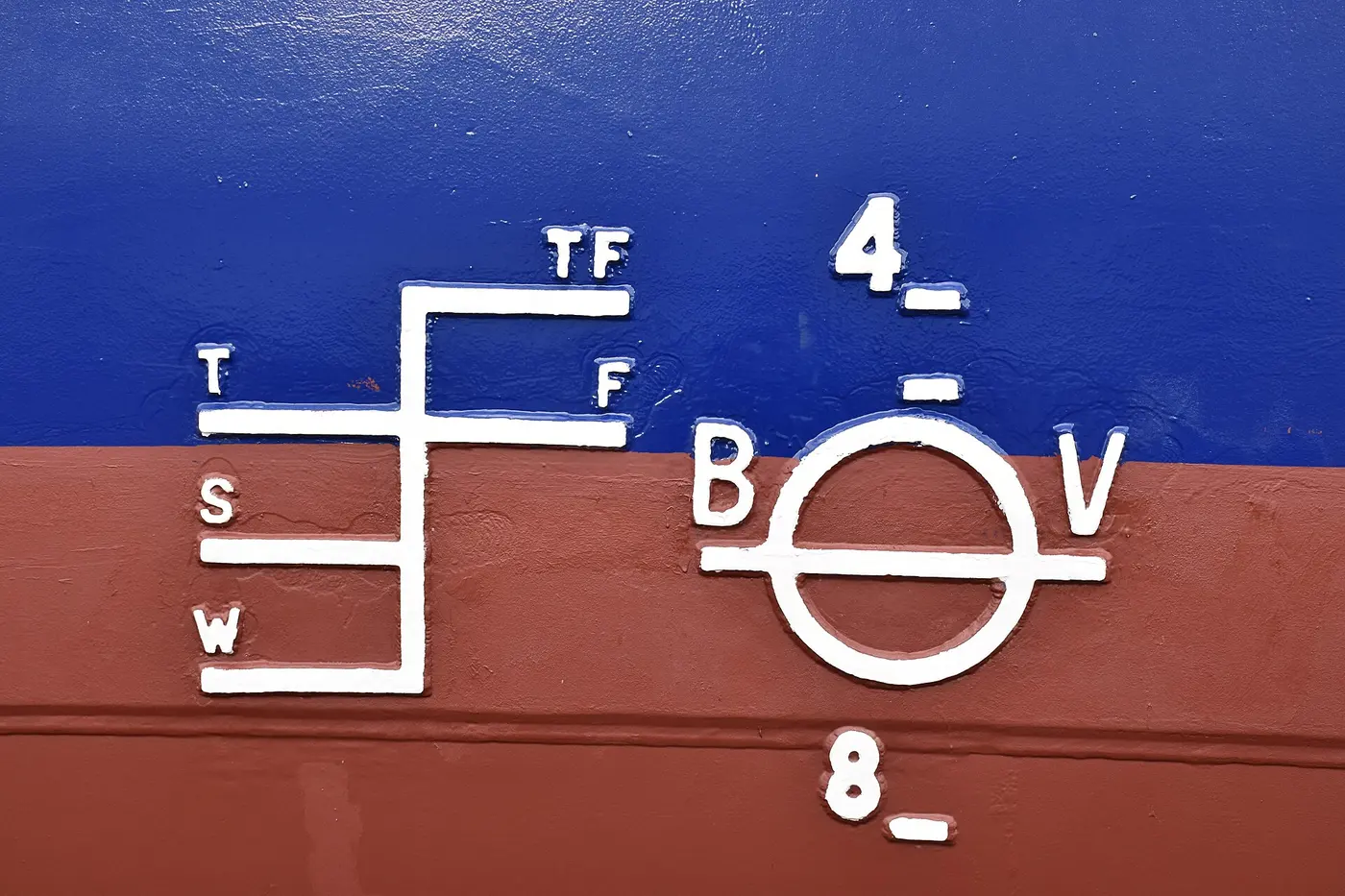 On the side of a hull painted red and blue, a white circle with a horizontal line and a set of lines labeled TF, F, T, S and W