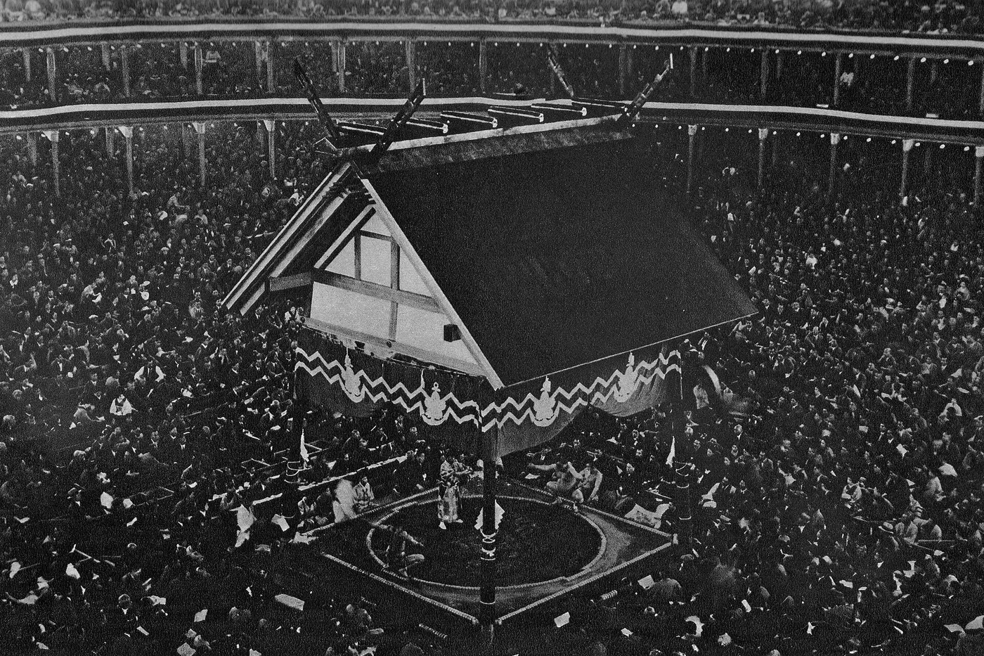 The ring at the old Ryōgoku Kokugikan, beneath a roof supported by four pillars, surrounded by a large crowd