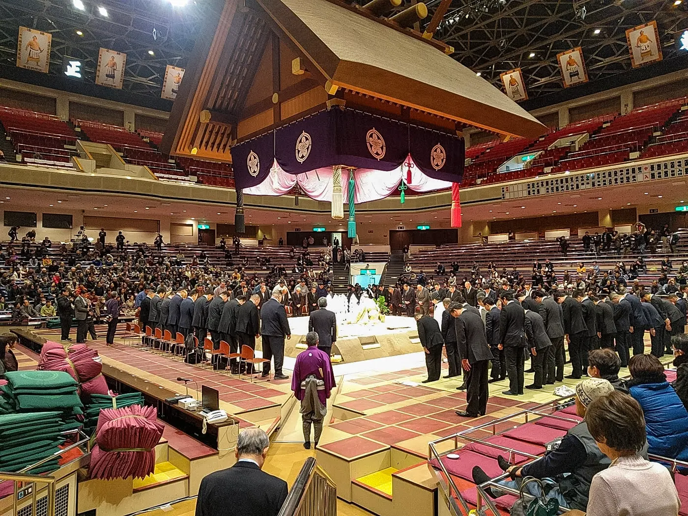 Officials bowing their heads around the ring beneath the suspended roof during the ring-blessing ceremony at the Ryōgoku Kokugikan