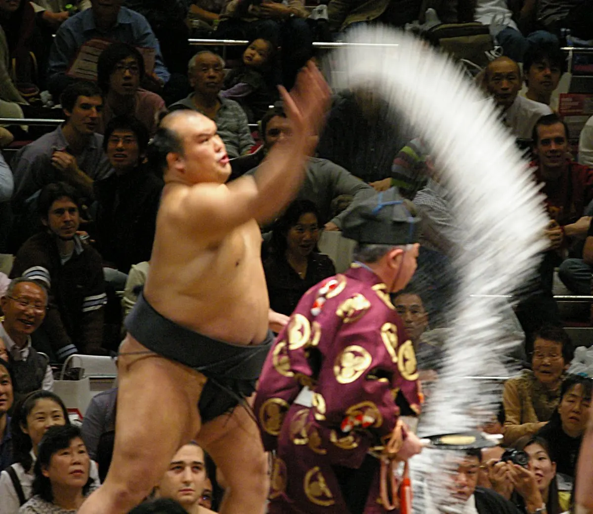 With spectators behind him, a wrestler swings his arm high as white salt fans out through the air