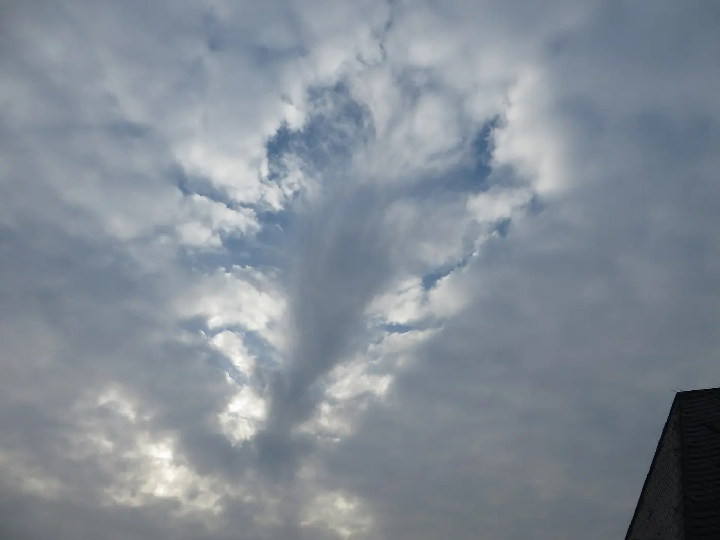 A sky covered in cloud with a large hole in it, with streaks hanging down from the center of the hole