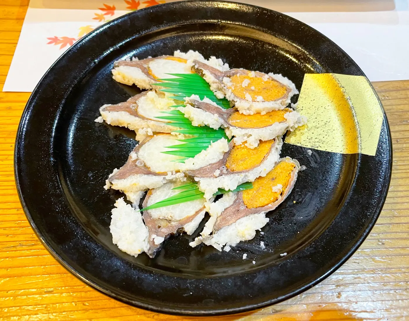 Slices of funazushi coated in white rice, arranged on a black plate