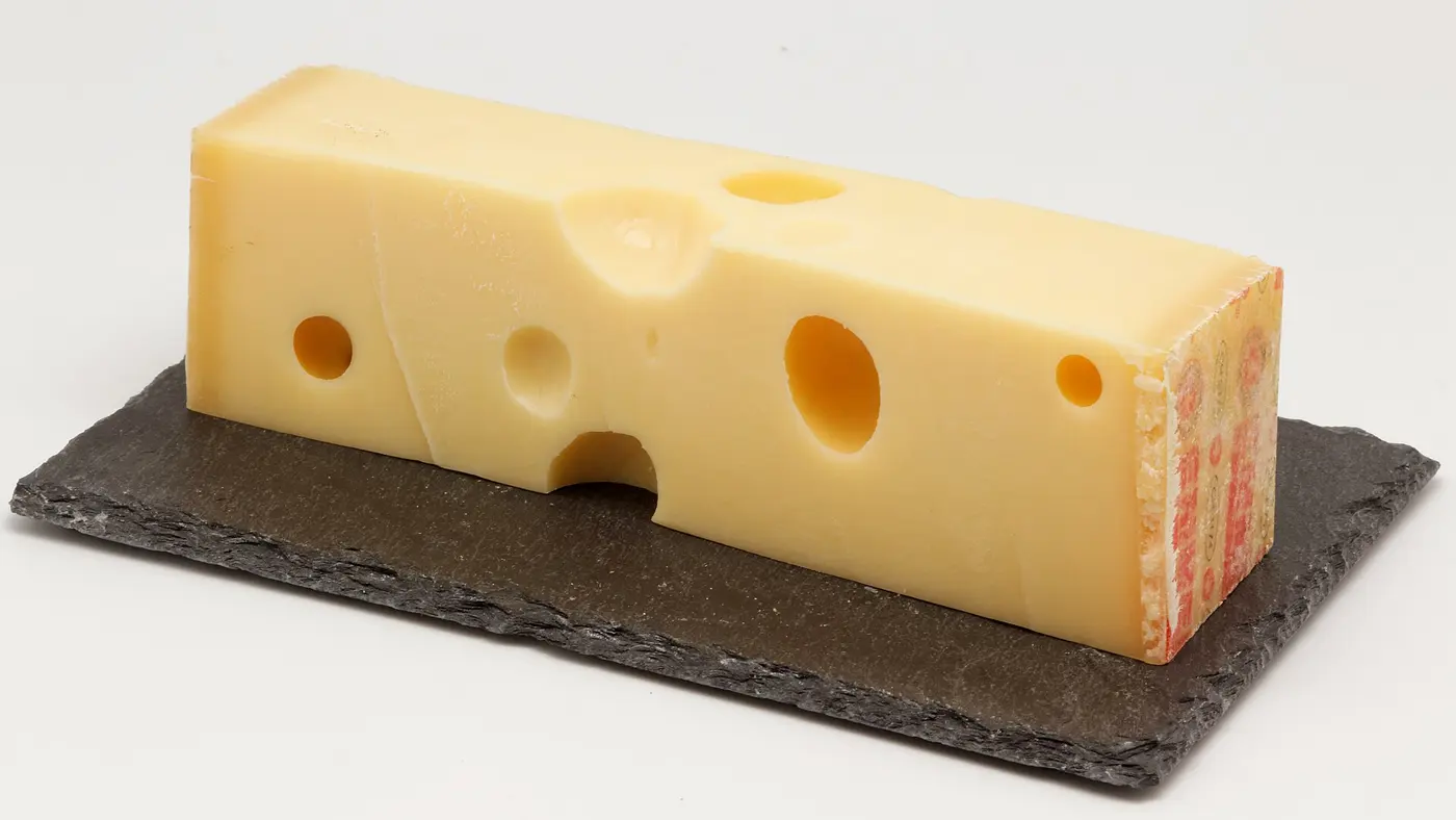 A long yellow block of cheese with several round holes, resting on a dark slate board