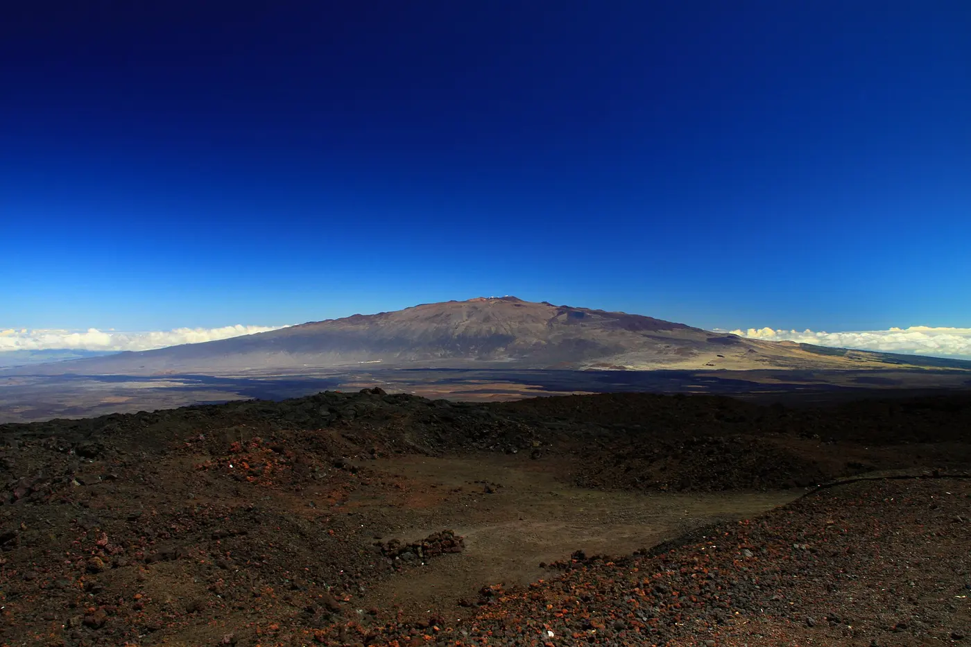 The broad, gently sloping profile of Mauna Kea stretching across the horizon under a blue sky