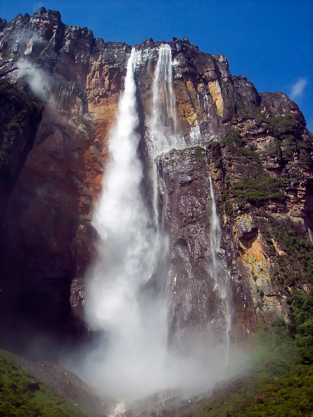 White water falling from the top of a sheer rock wall and spreading into mist at its base
