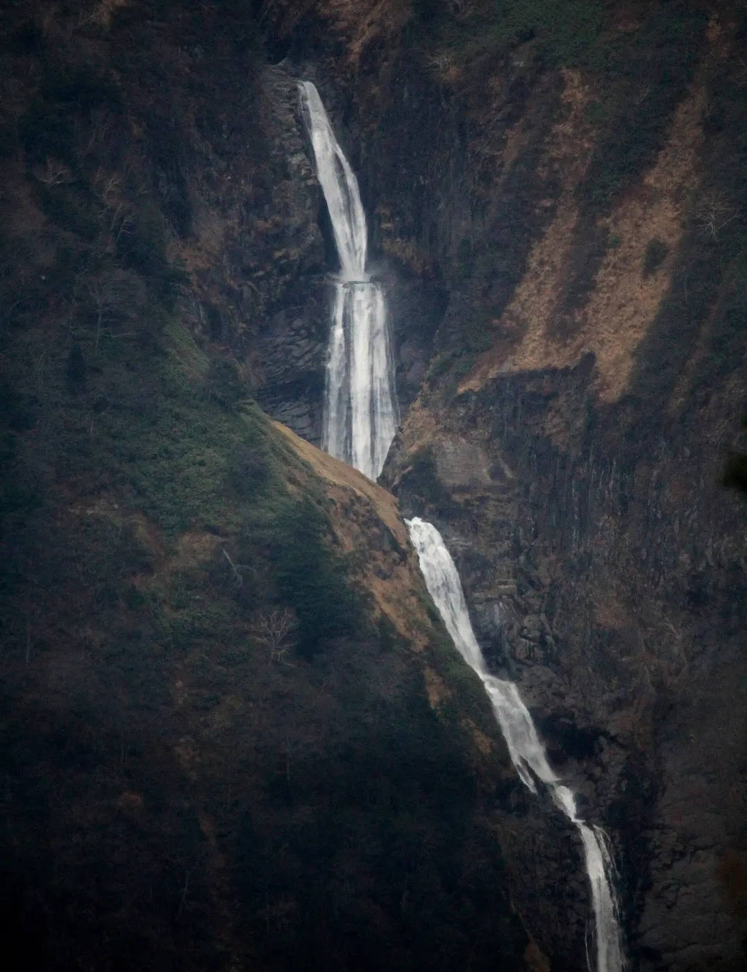 A waterfall descending in several tiers through a deep valley of brown and green mountainsides