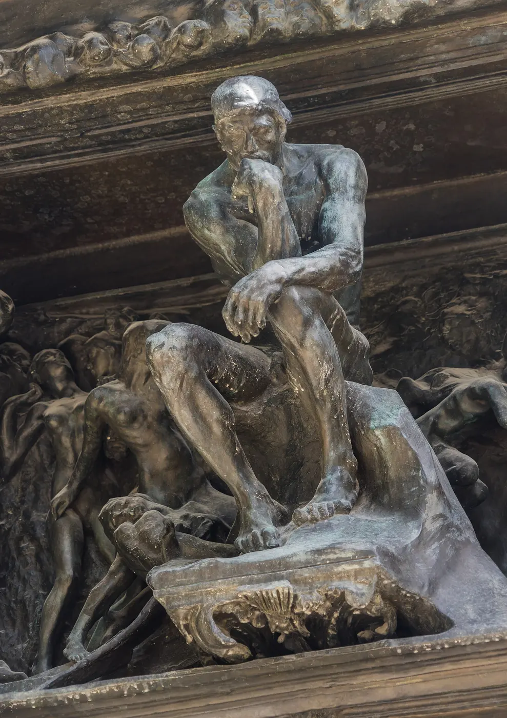 A figure bent in thought at the top of a gateway, surrounded by crowds of other figures
