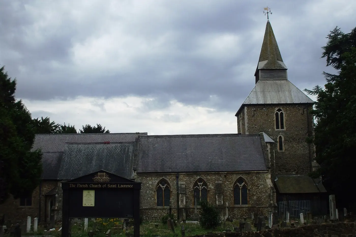 A small church with stone walls and a pointed wooden spire under a cloudy sky