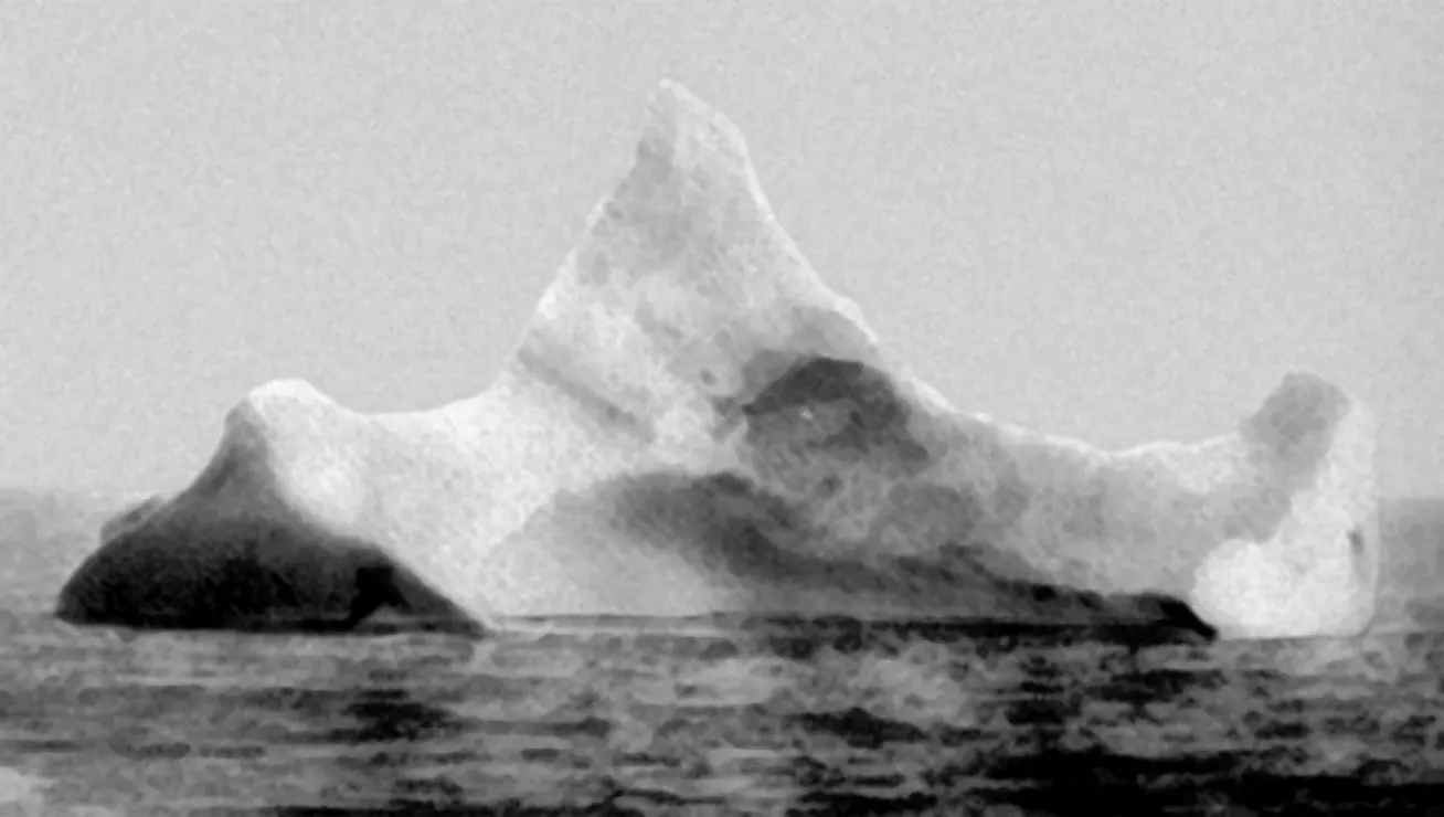 A black-and-white photo of an iceberg shaped like a jagged mountain floating in the sea