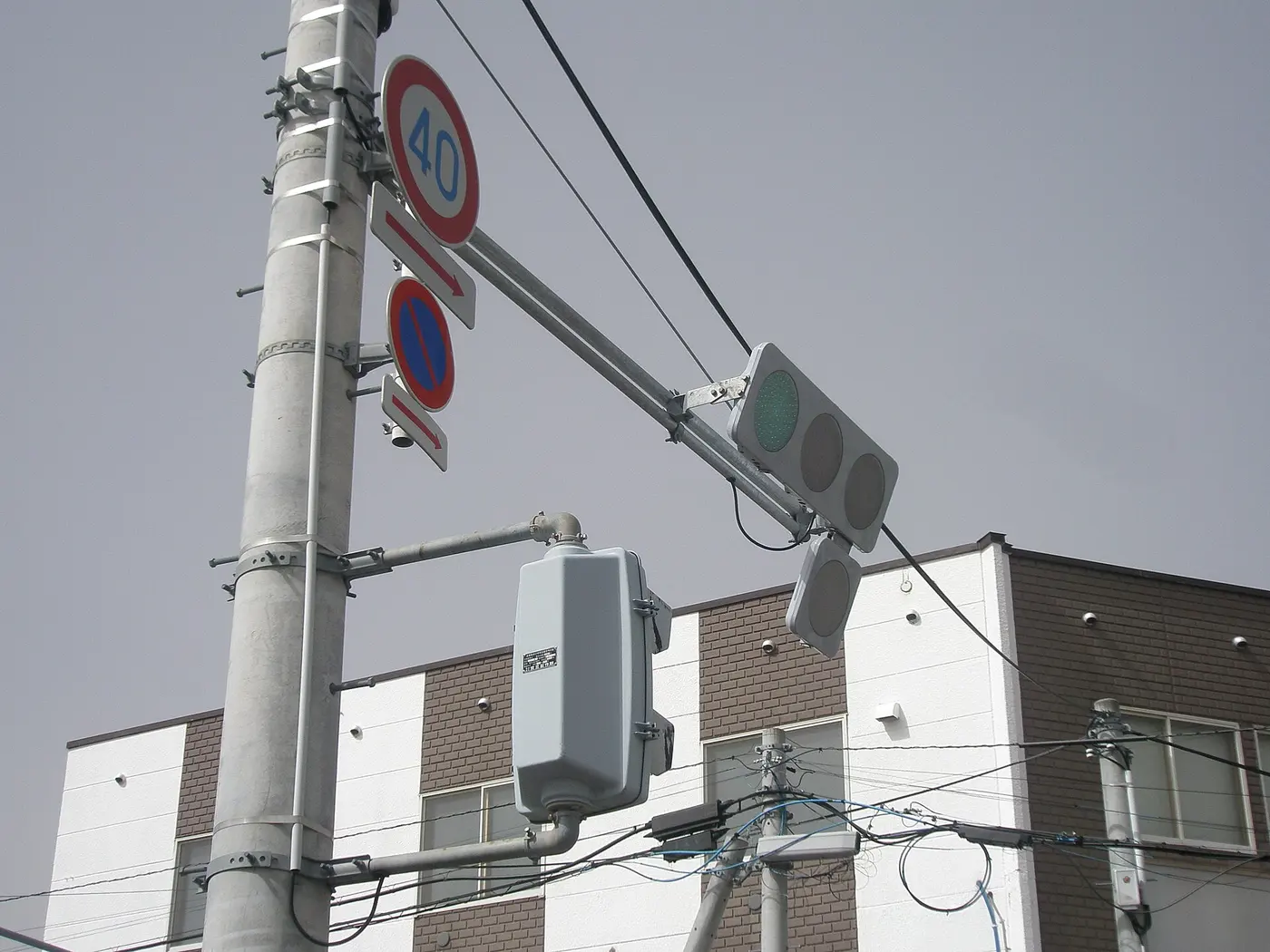 A Japanese traffic light on an arm extending from a utility pole, with the leftmost of three horizontally arranged lamps glowing green