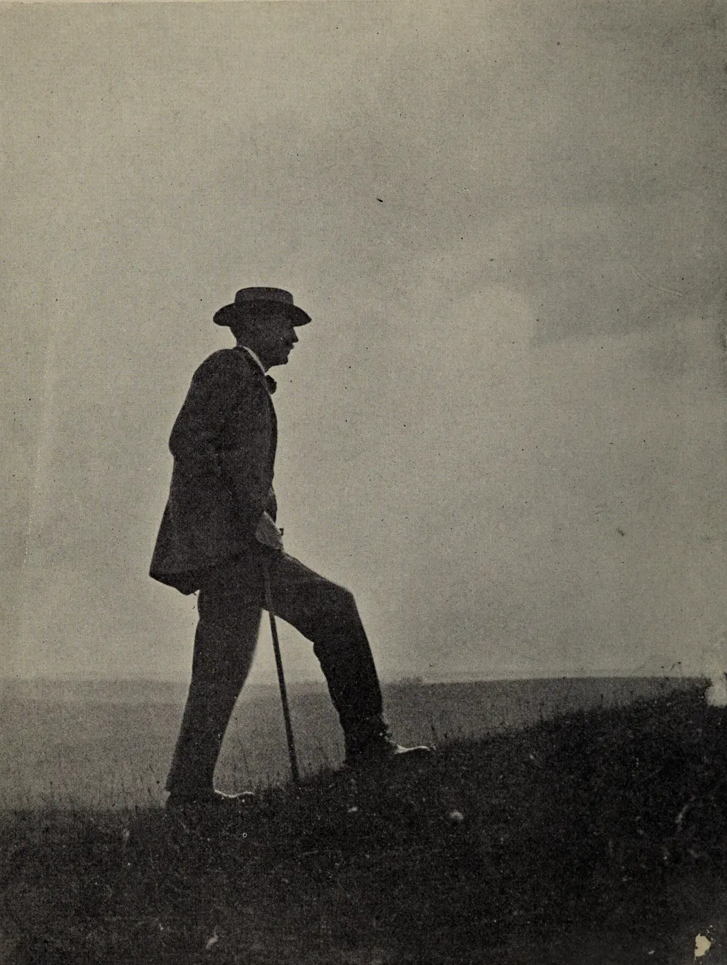 Silhouette of a man in a hat, leaning on a walking stick on a grassy slope
